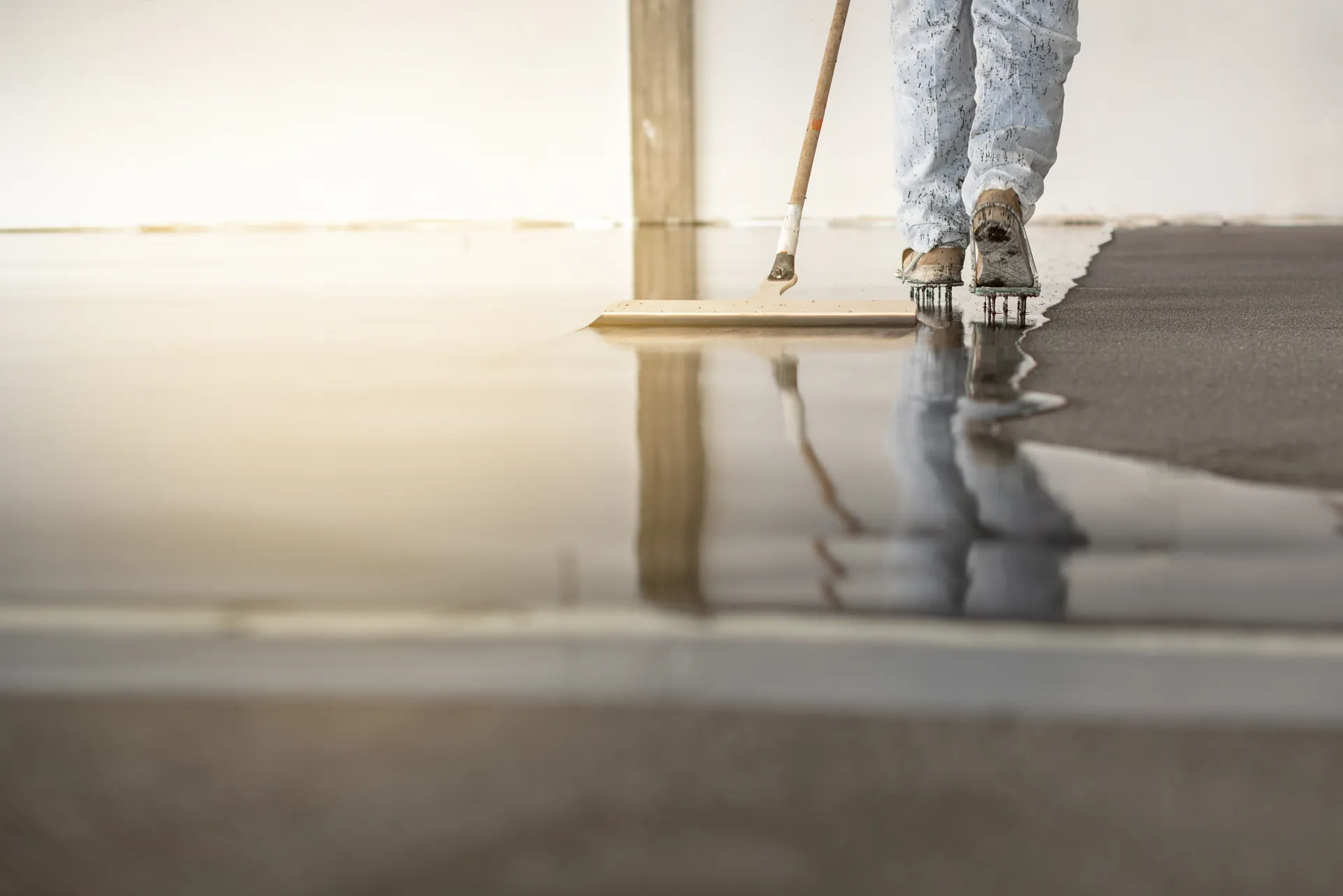 Professional applying epoxy floor coating with spiked shoes
